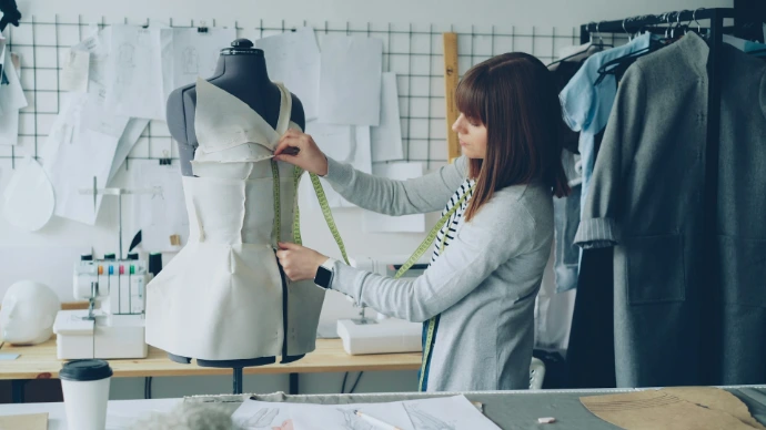 A fashion designer measures a garment on a mannequin.